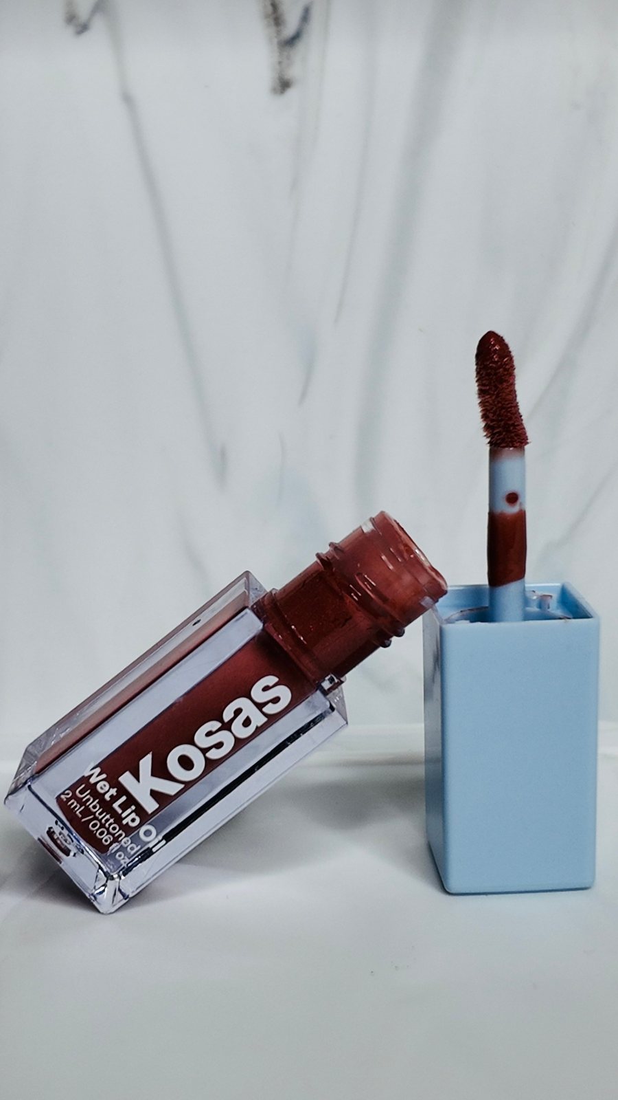 Lip gloss product detail shot on a neutral surface