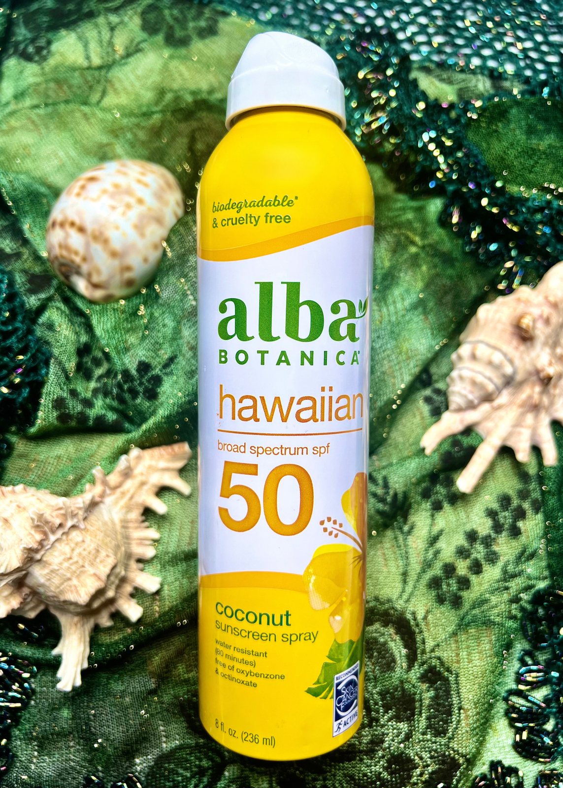 Sunscreen spray styled with shells on a green textile